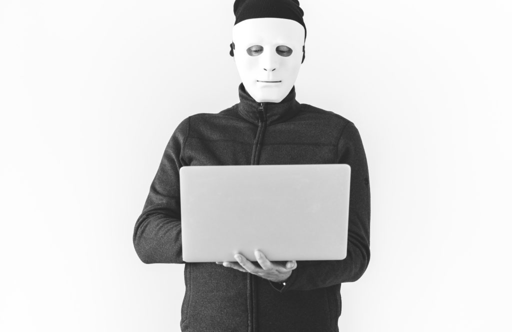 computer hacker wearing white mask and holding laptop